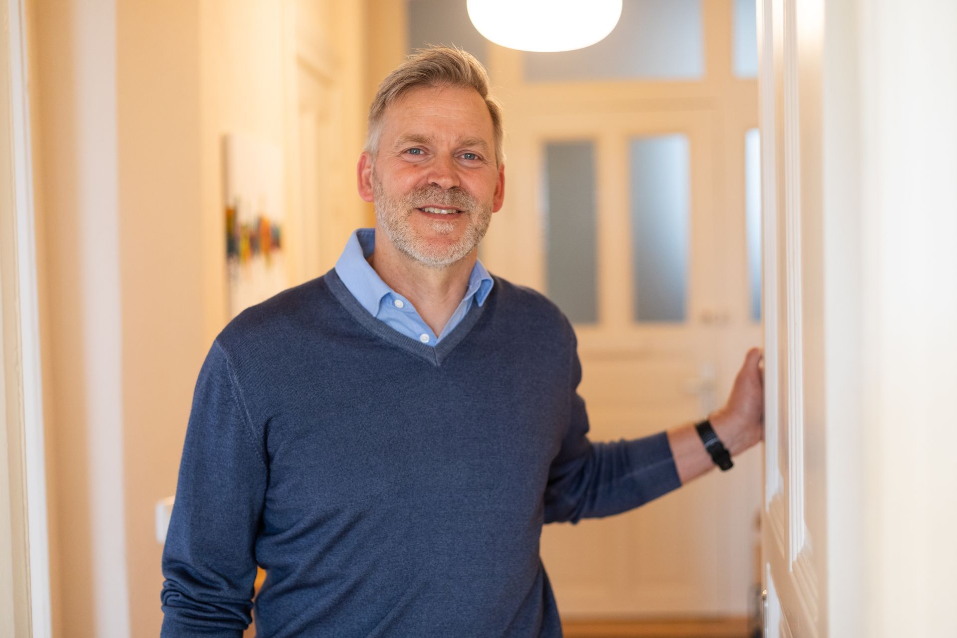 Ein Mann in einem blauen Pullover sitzt an einem Tisch vor einem Fenster.