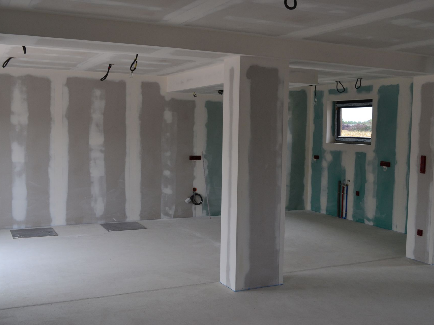 Pièce inachevée avec cloisons sèches, sol blanc et fenêtre sur un chantier de rénovation.