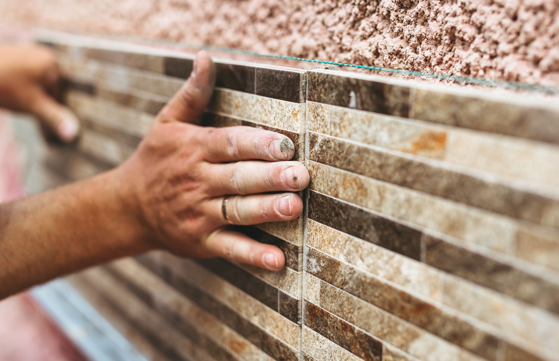 Des mains posent des carreaux de faïence beiges et marron sur un mur.