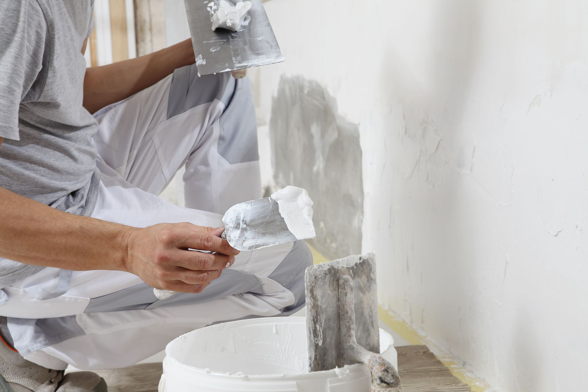 Une personne lisse du plâtre sur un mur à l'aide d'un couteau et d'un bac.