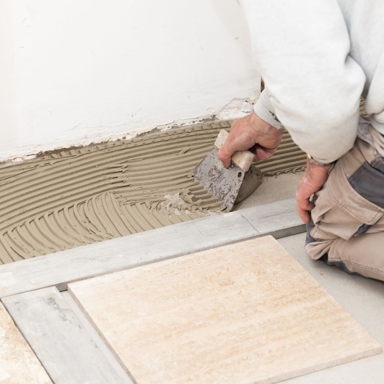 Une personne étale de la colle sur un sol lors de la pose de carrelage.