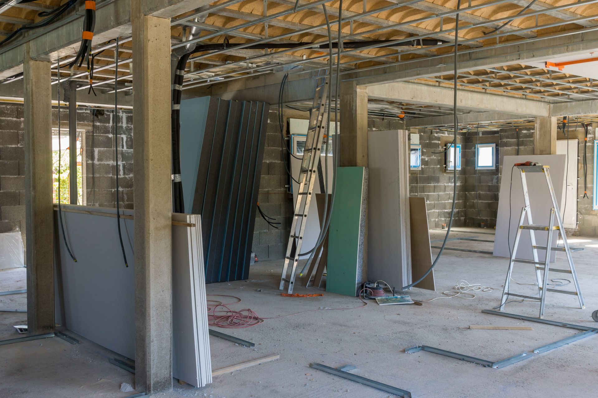 Intérieur en travaux avec structures de faux plafond apparentes, panneaux de plaques de plâtre, échelles et outils éparpillés.