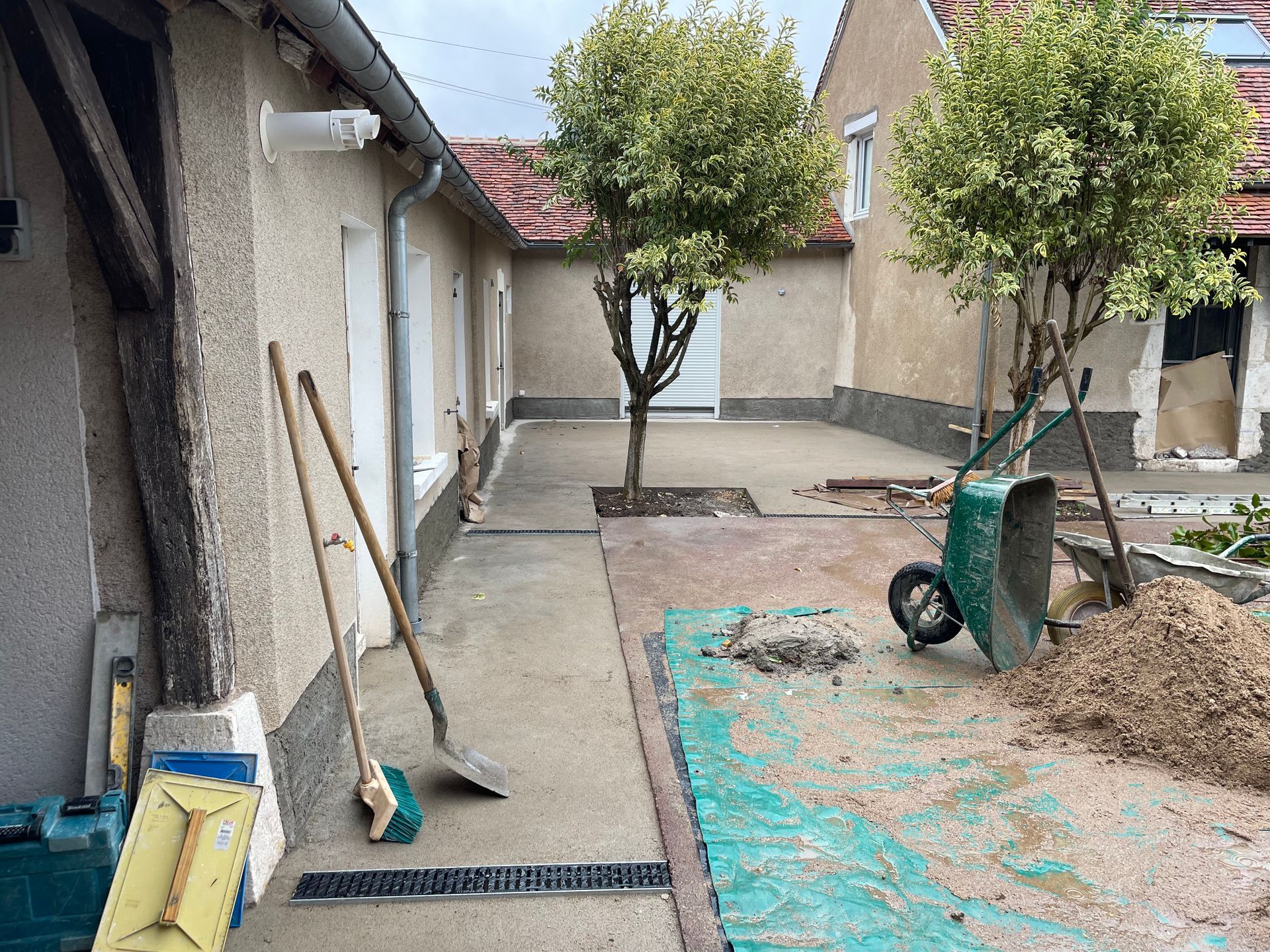 Cour arrière avec deux arbres, une brouette et des matériaux de construction.