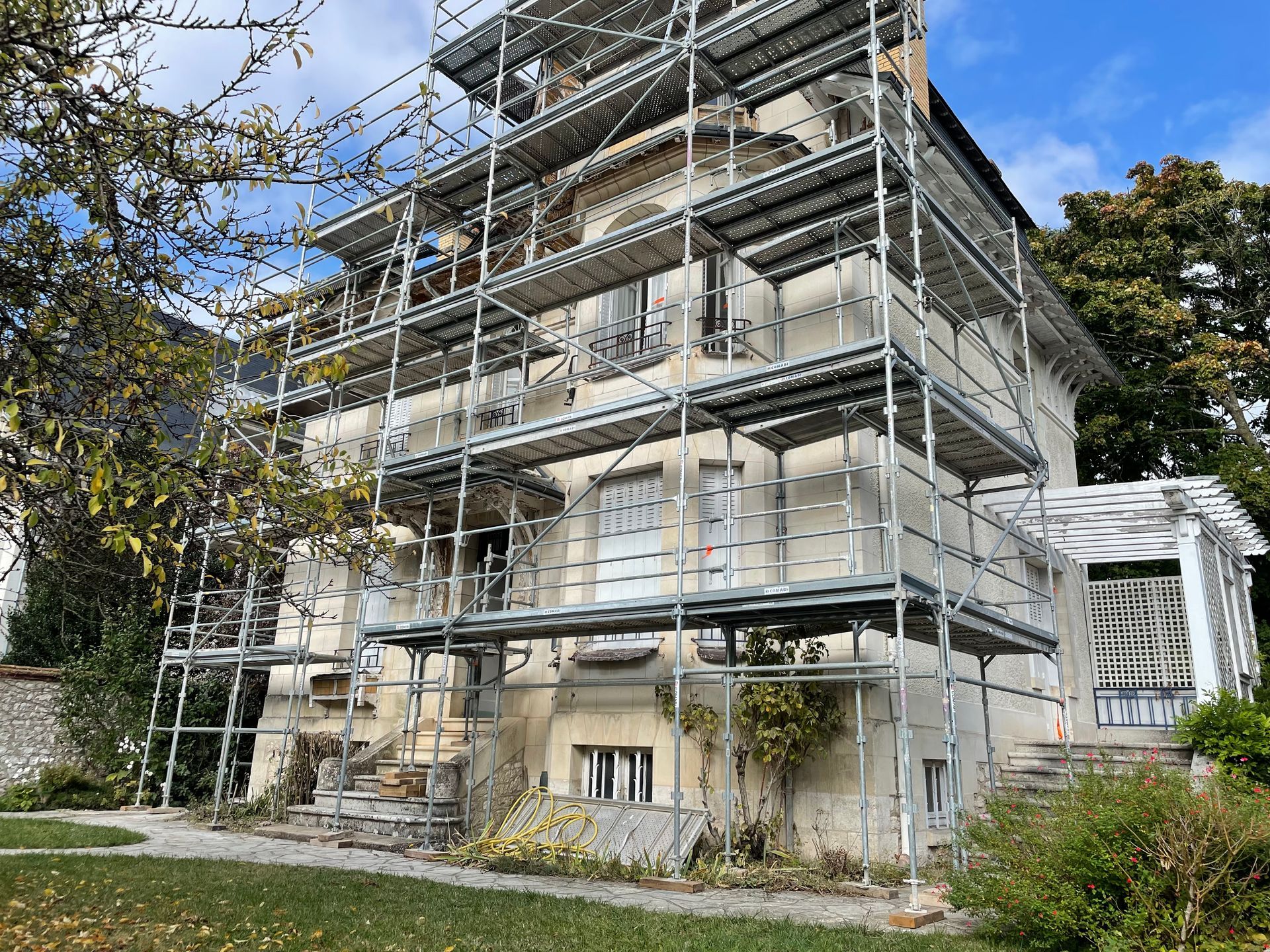 Maison ancienne à plusieurs étages en rénovation, recouvert d'un échafaudage et entouré d'arbres.