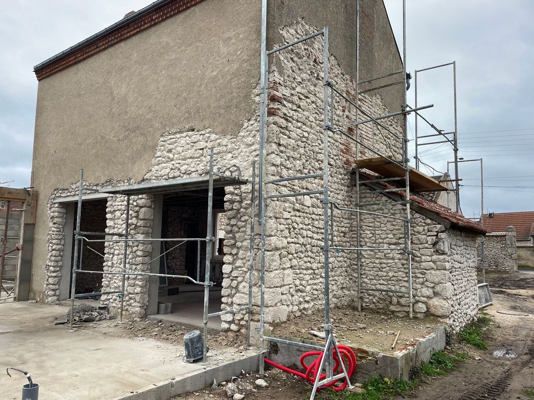Maison en pierre en rénovation, avec échafaudages et maçonnerie apparente.