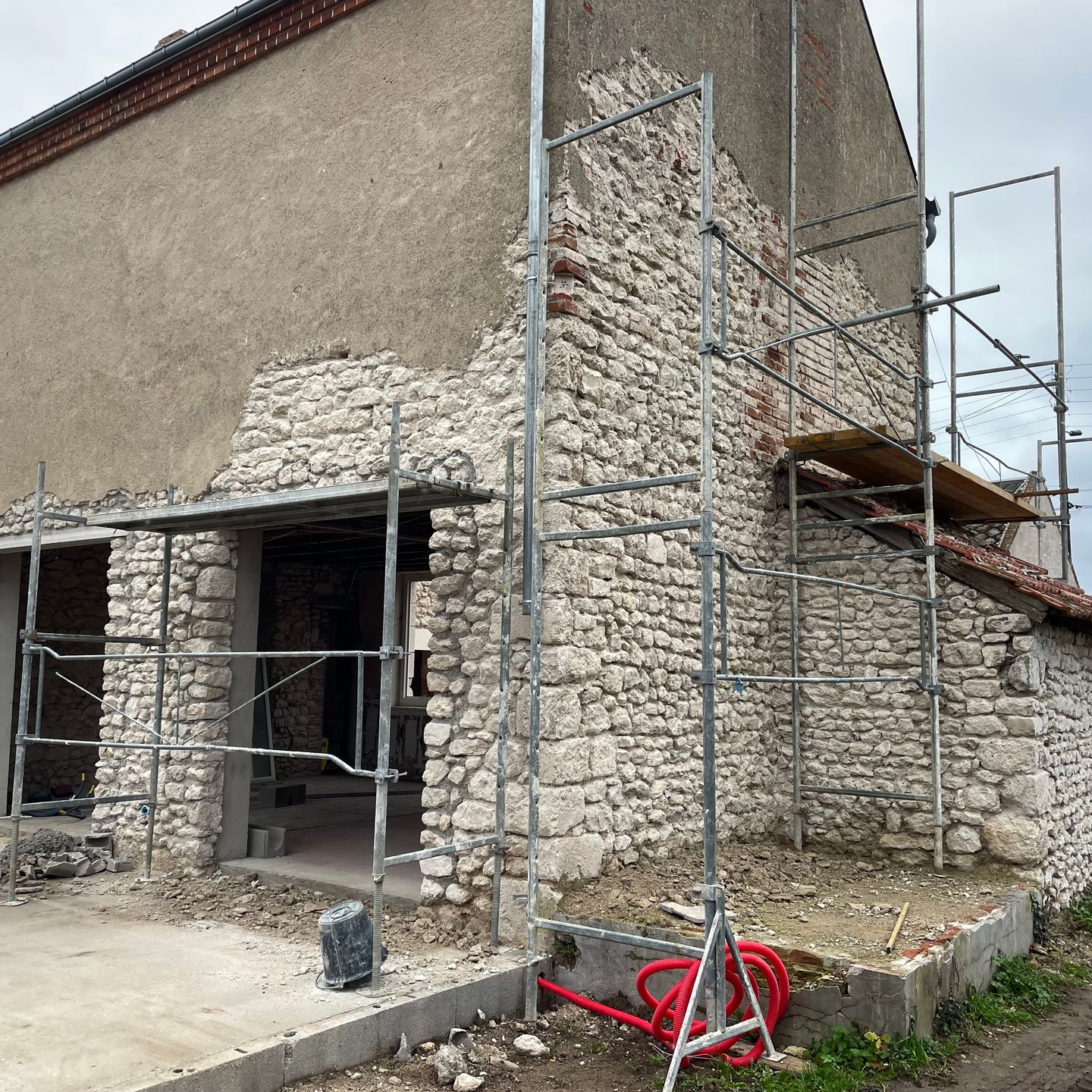 Maison en pierre en cours de rénovation, avec des échafaudages autour de l'entrée et du mur latéral.