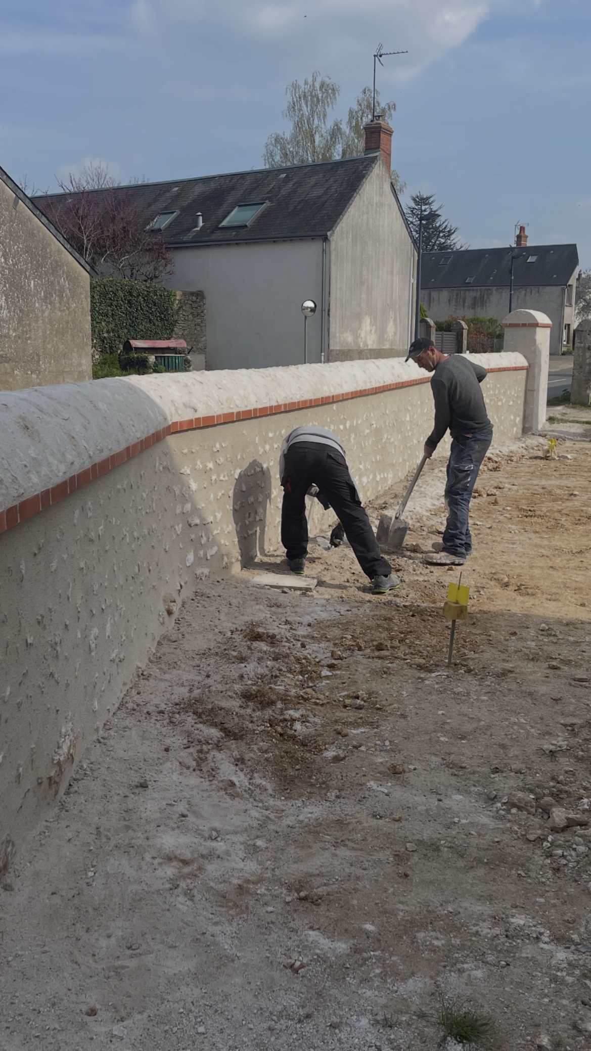 Deux ouvriers étalent du béton frais le long d'un mur blanc sur un chantier.