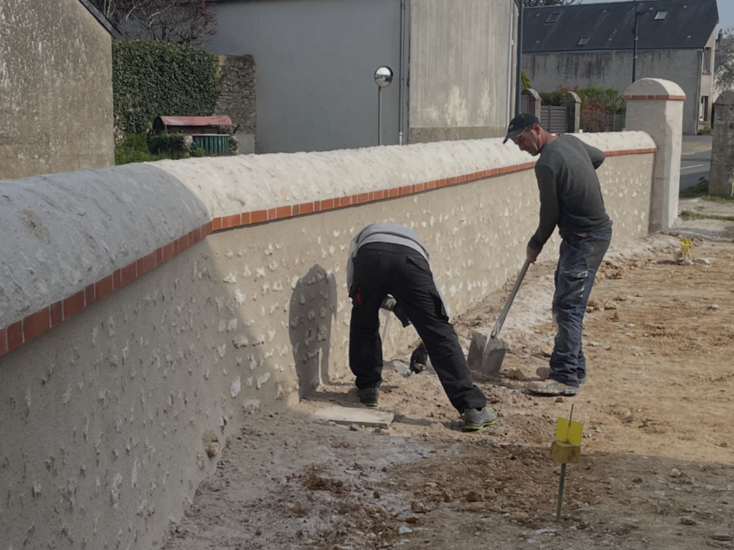 Deux ouvriers réparent un mur de pierre percé d'une ouverture cintrée sur un chantier de construction.