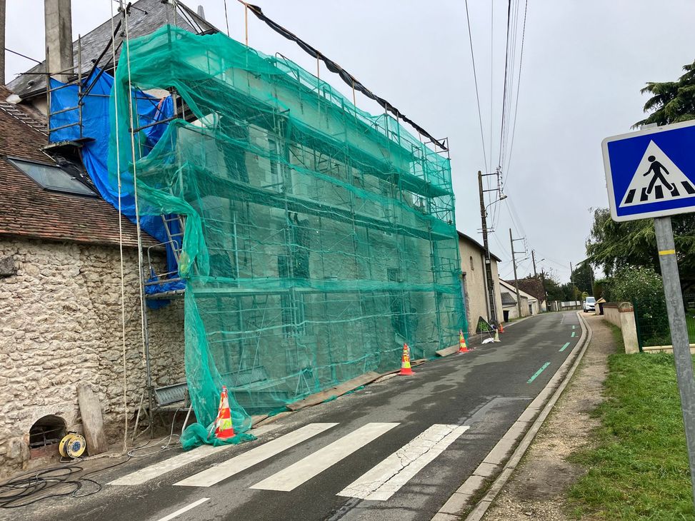 Rue avec un bâtiment sous des filets d'échafaudage verts et des cônes de signalisation à côté d'un passage piéton.