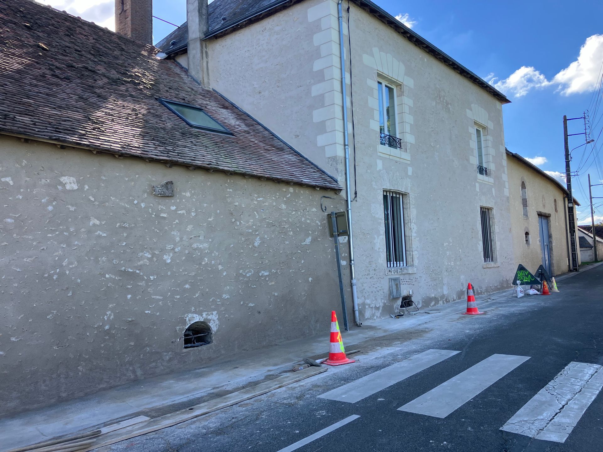 Rue étroite bordée de vieux bâtiments en pierre, avec des passages piétons et des cônes de signalisation orange.
