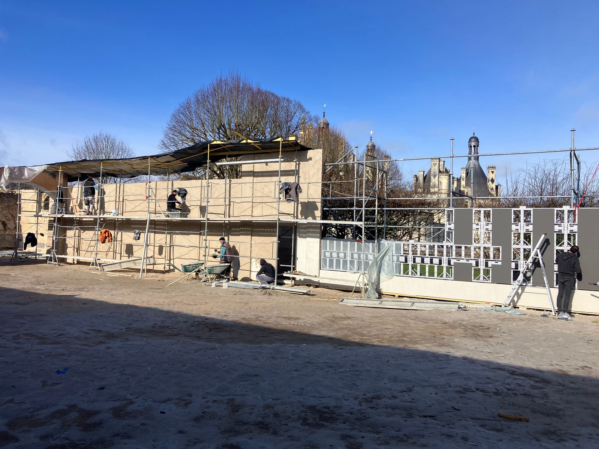 Chantier de clôture d'un château avec échafaudages, gravats et un ciel bleu dégagé.