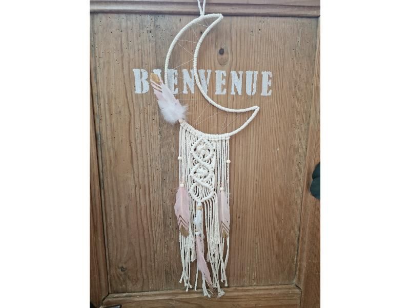 Un attrape-rêves avec un croissant de lune et des plumes est accroché à une porte en bois.