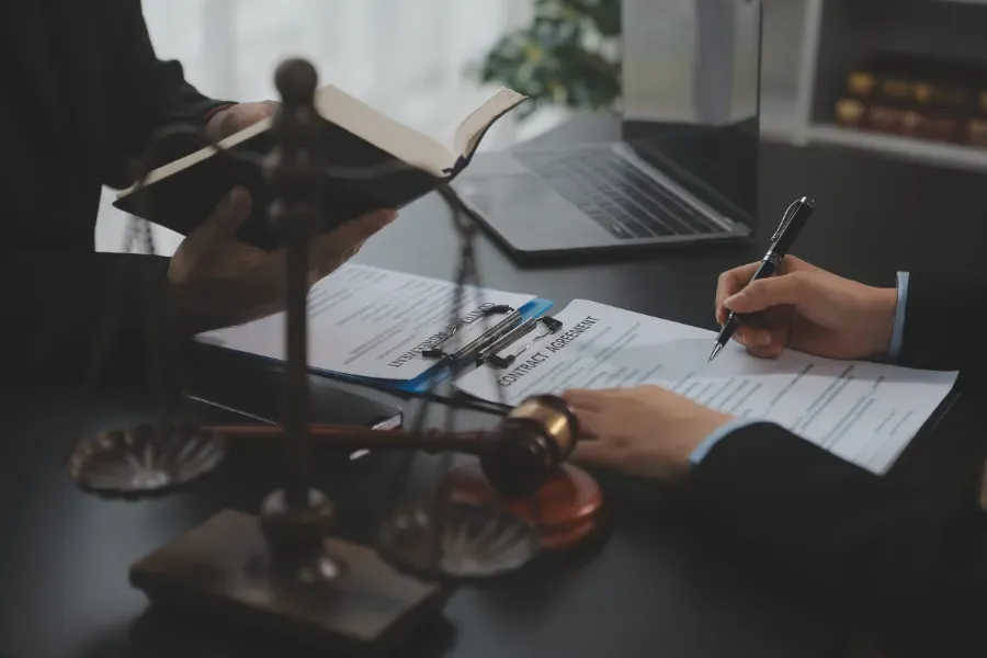 Personas firmando documentos en una mesa con una computadora portátil y una balanza de la justicia.