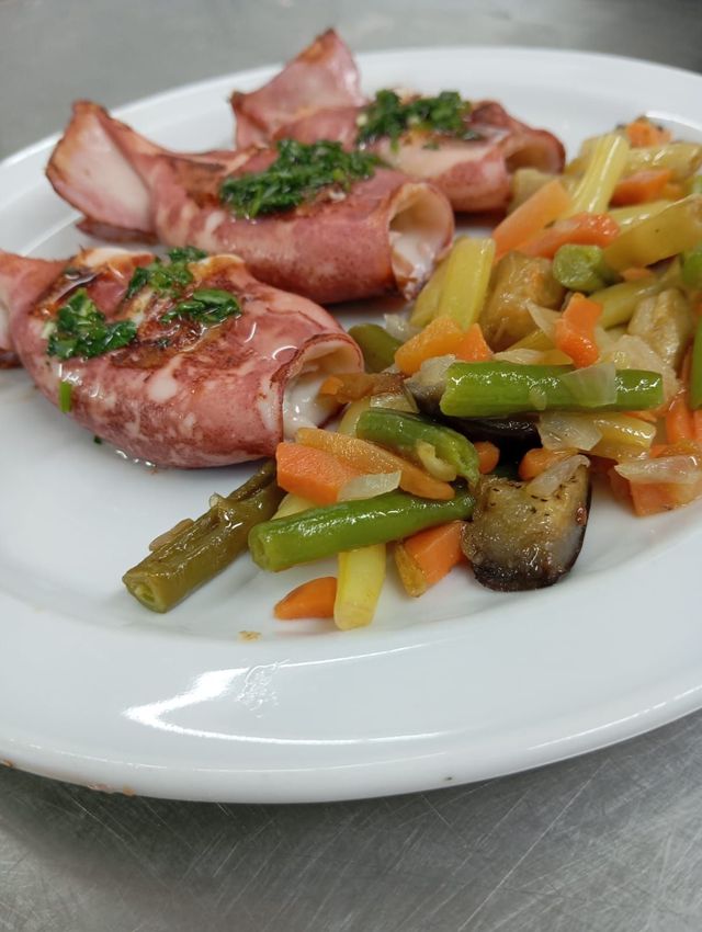 Un plato blanco cubierto con carne y verduras sobre una mesa.