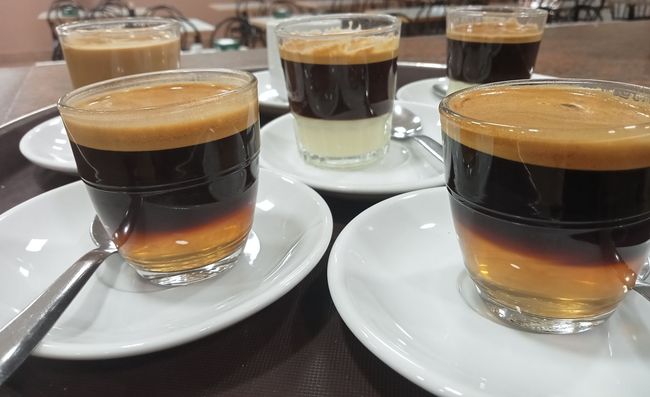 Cuatro tazas de café en platillos con cucharas en una bandeja