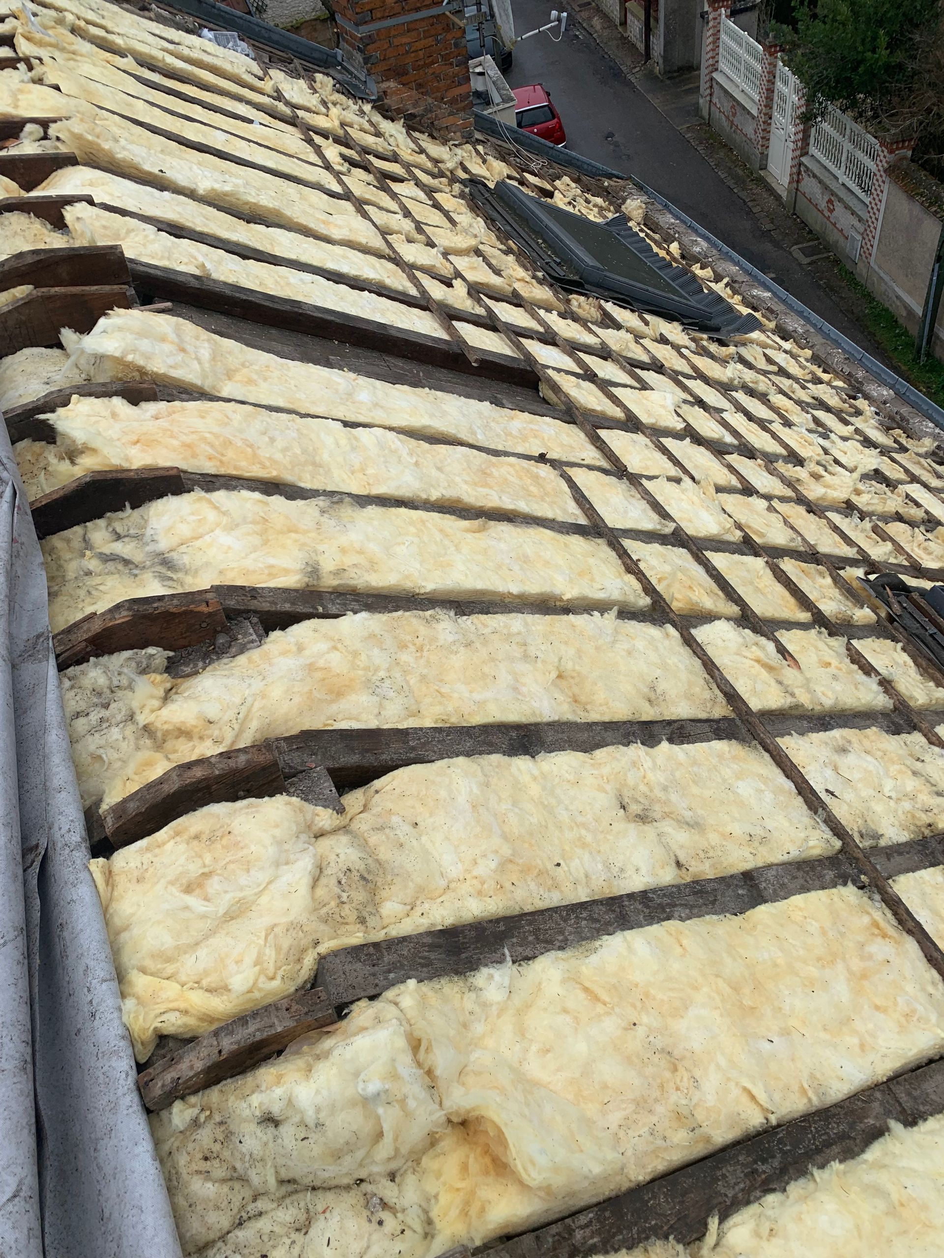 Des rangées de matériaux de couverture clairs, fixés par des bandes sombres, sur un toit en pente près d'une rue et d'un mur.