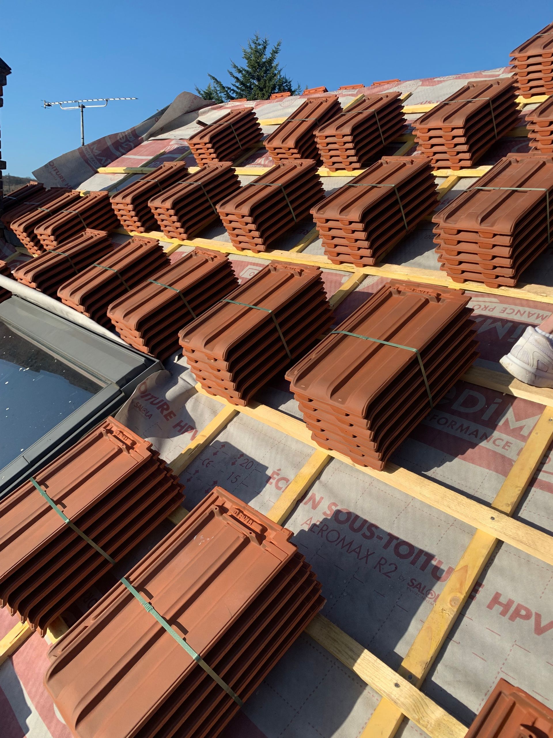 Des piles de tuiles rouges disposées sur un toit sous un ciel bleu dégagé.
