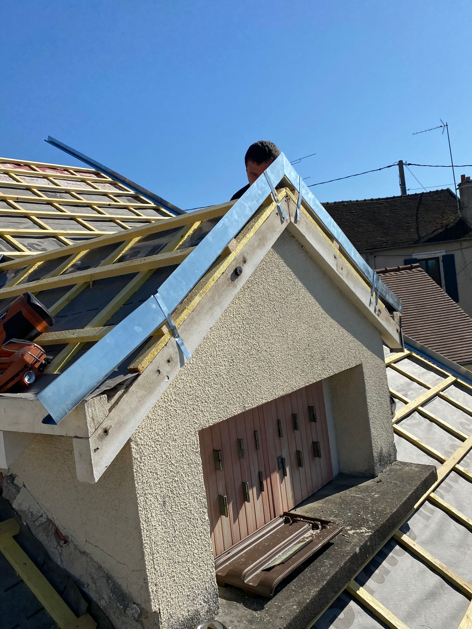 Petite lucarne sur le toit d'une maison, avec des tuiles inachevées et une fenêtre condamnée.