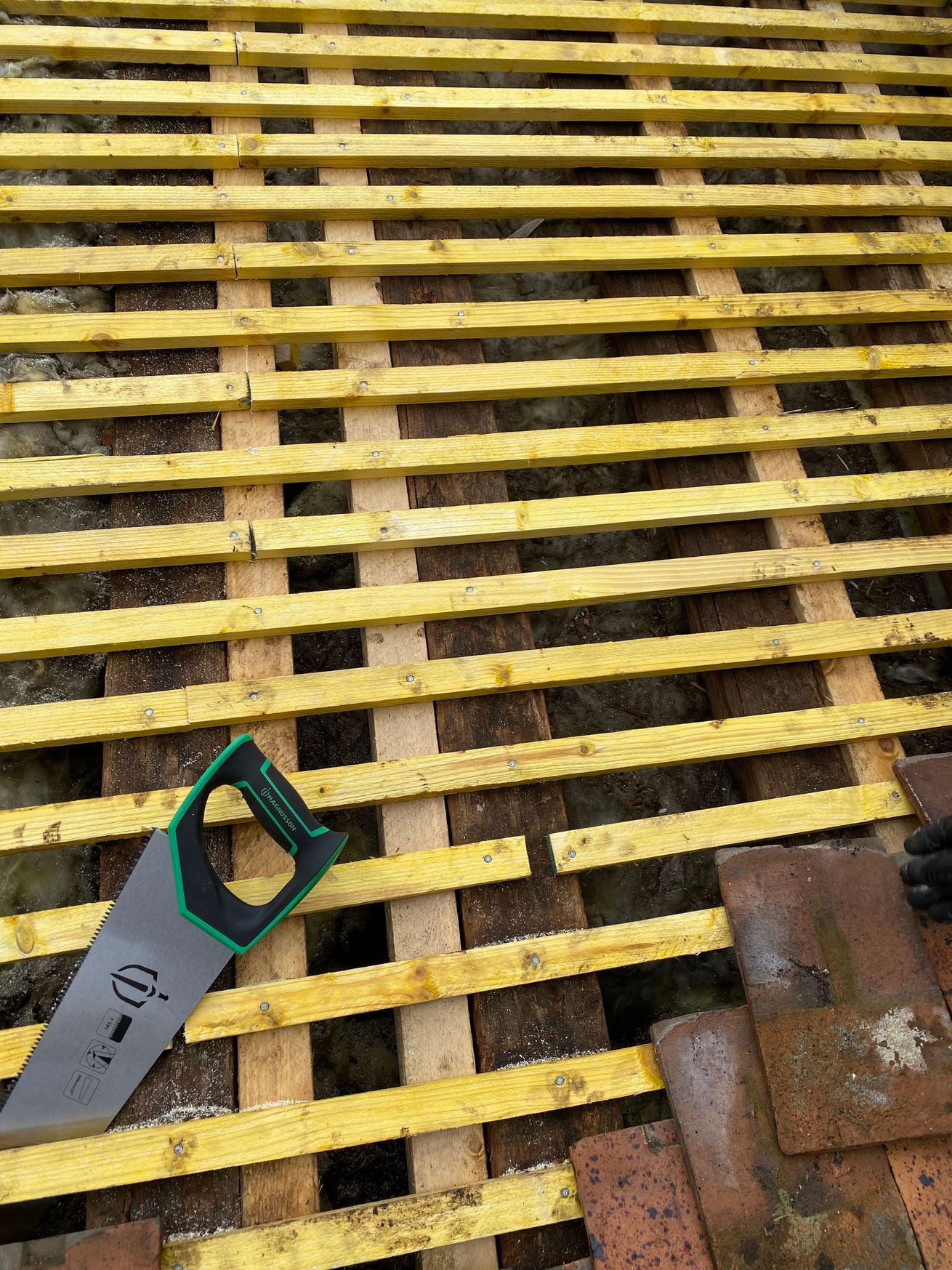 Surface en lattes de bois jaune avec un outil à main à manche vert et une pièce de métal rouillée dans le coin
