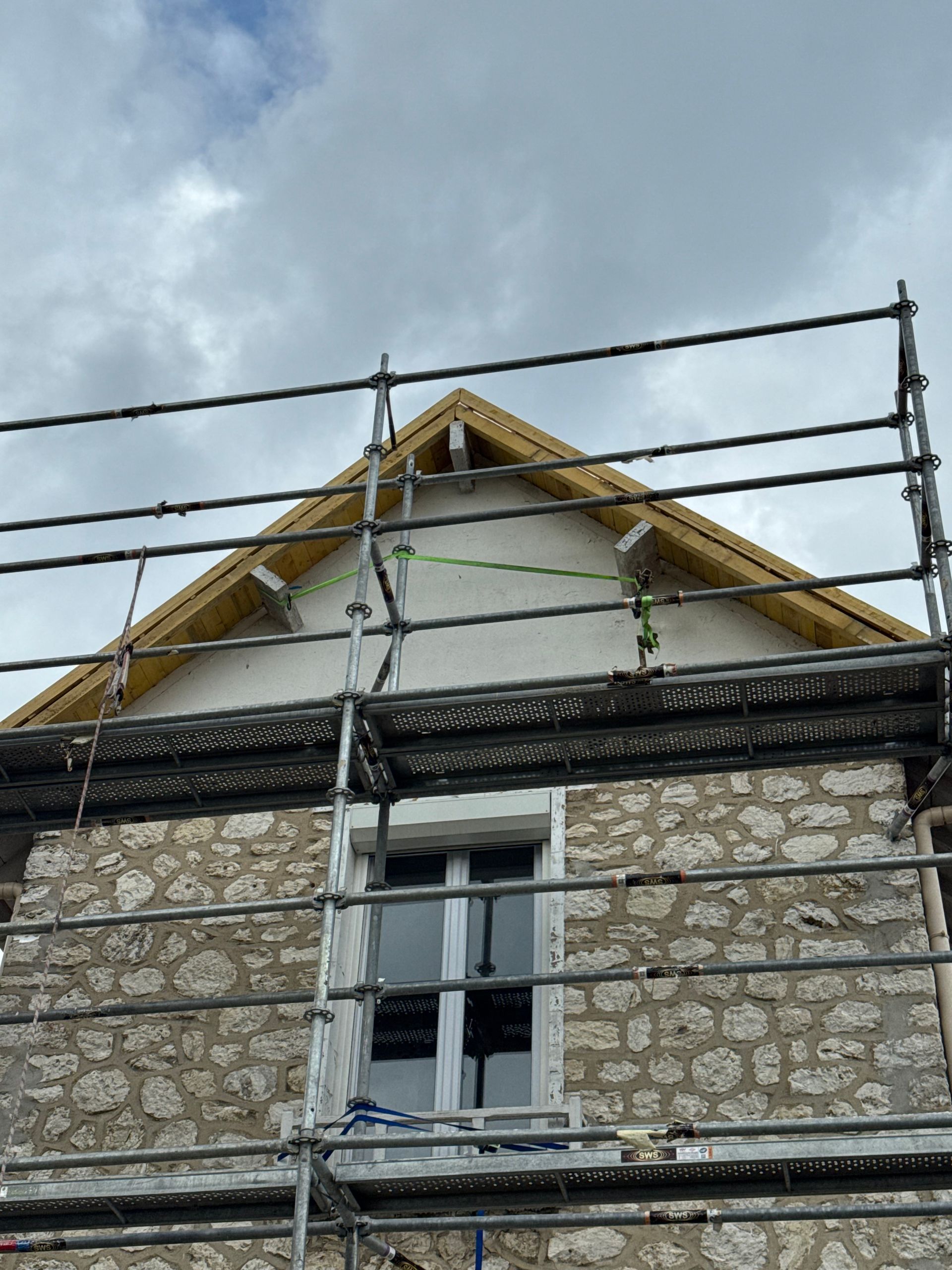 Façade de maison en pierre avec échafaudages sous un ciel nuageux