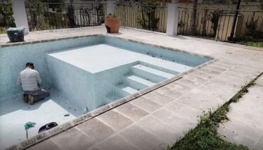 Un hombre está arrodillado al borde de una piscina.
