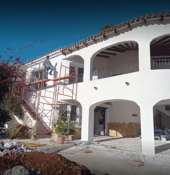 Un hombre subido a un andamio está pintando una gran casa blanca.