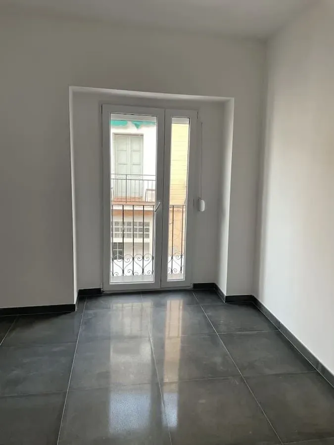 Una habitación vacía con un balcón y una puerta corrediza de vidrio.