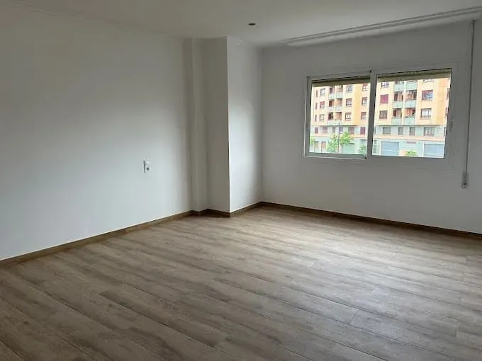 Una habitación vacía con suelo de madera y dos ventanas.