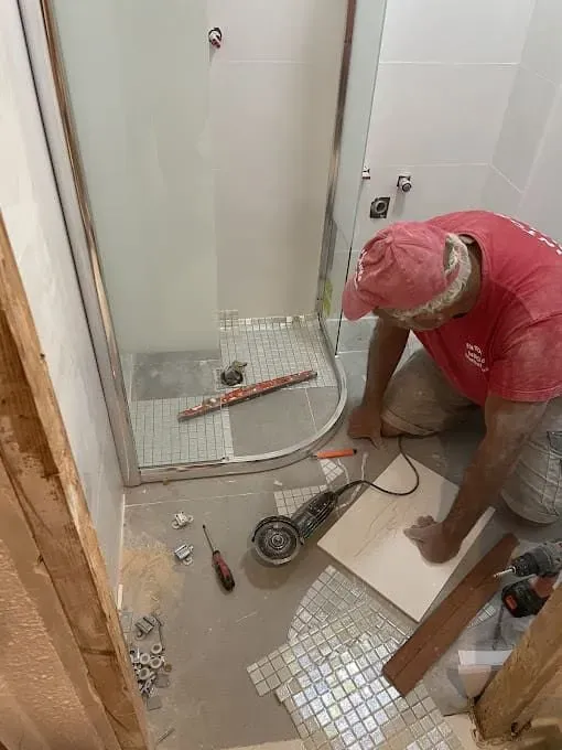 Un hombre está trabajando en un piso de baldosas en un baño.