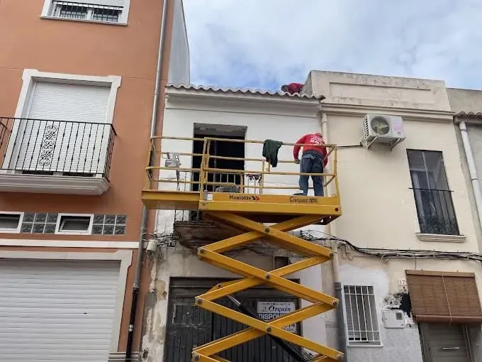 Un hombre está parado en un elevador de tijera amarillo frente a un edificio.