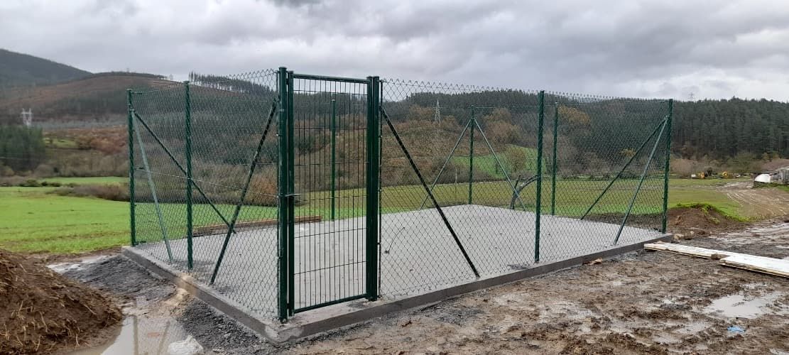 Una valla con una puerta en medio de un campo fangoso.