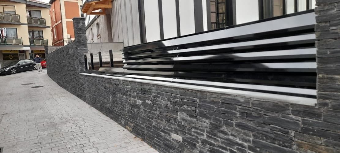 Un muro de piedra está rodeado por una valla metálica al costado de una calle.