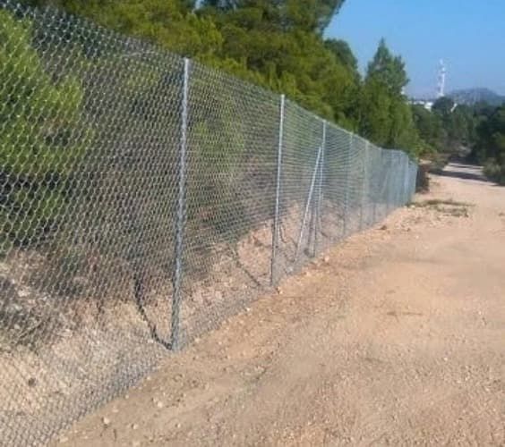 Una cerca de alambre de cadena está a lo largo del costado de un camino de tierra.