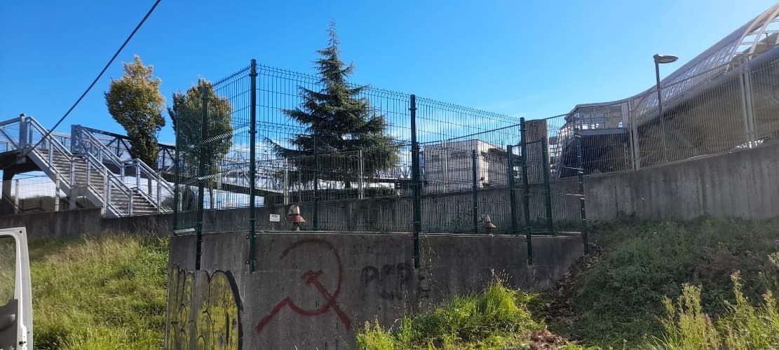 Una valla con grafitis y un puente al fondo.