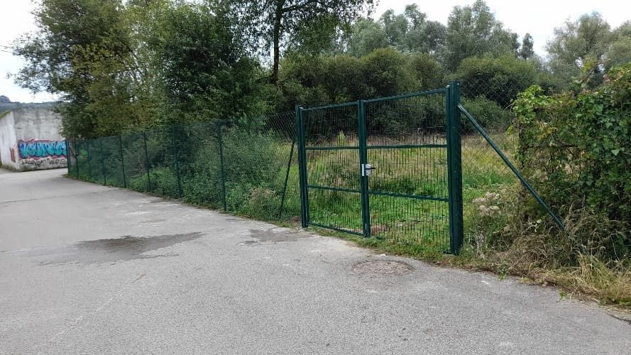 Una valla con una puerta en medio de un camino rodeado de árboles.