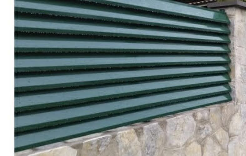 Una valla metálica verde se encuentra encima de un muro de piedra.