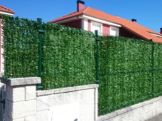 Una valla verde con una casa al fondo.