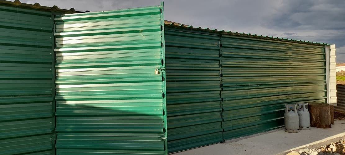 Una valla metálica verde con una puerta abierta.