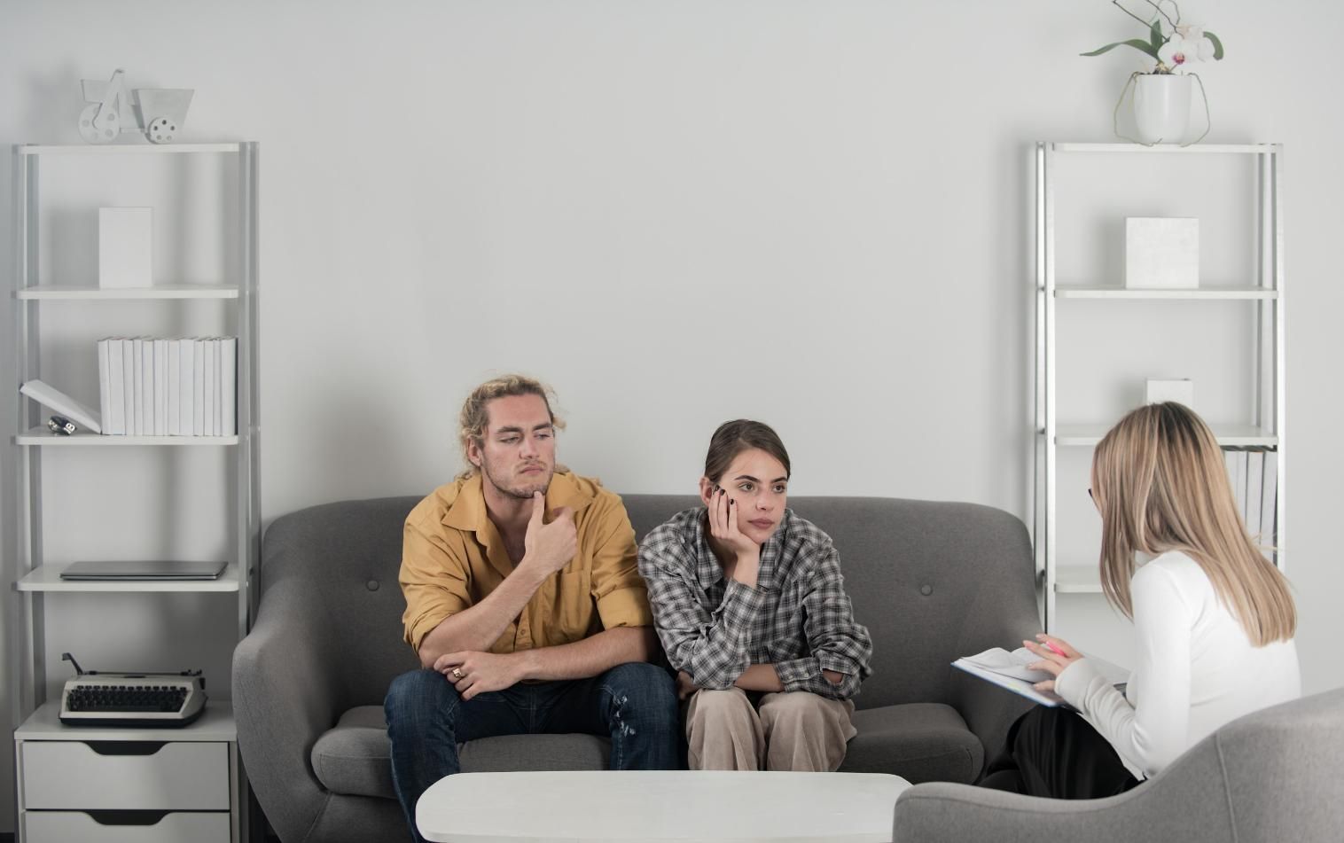 La pareja se sienta en el sofá en una sesión de terapia, luciendo angustiada; el terapeuta toma notas.