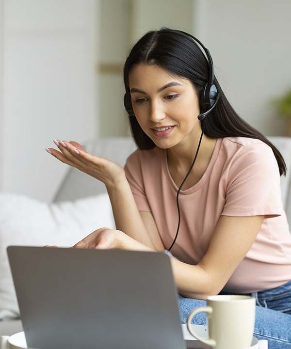 Una mujer con auriculares hace gestos mientras realiza una videollamada desde su ordenador portátil en casa.