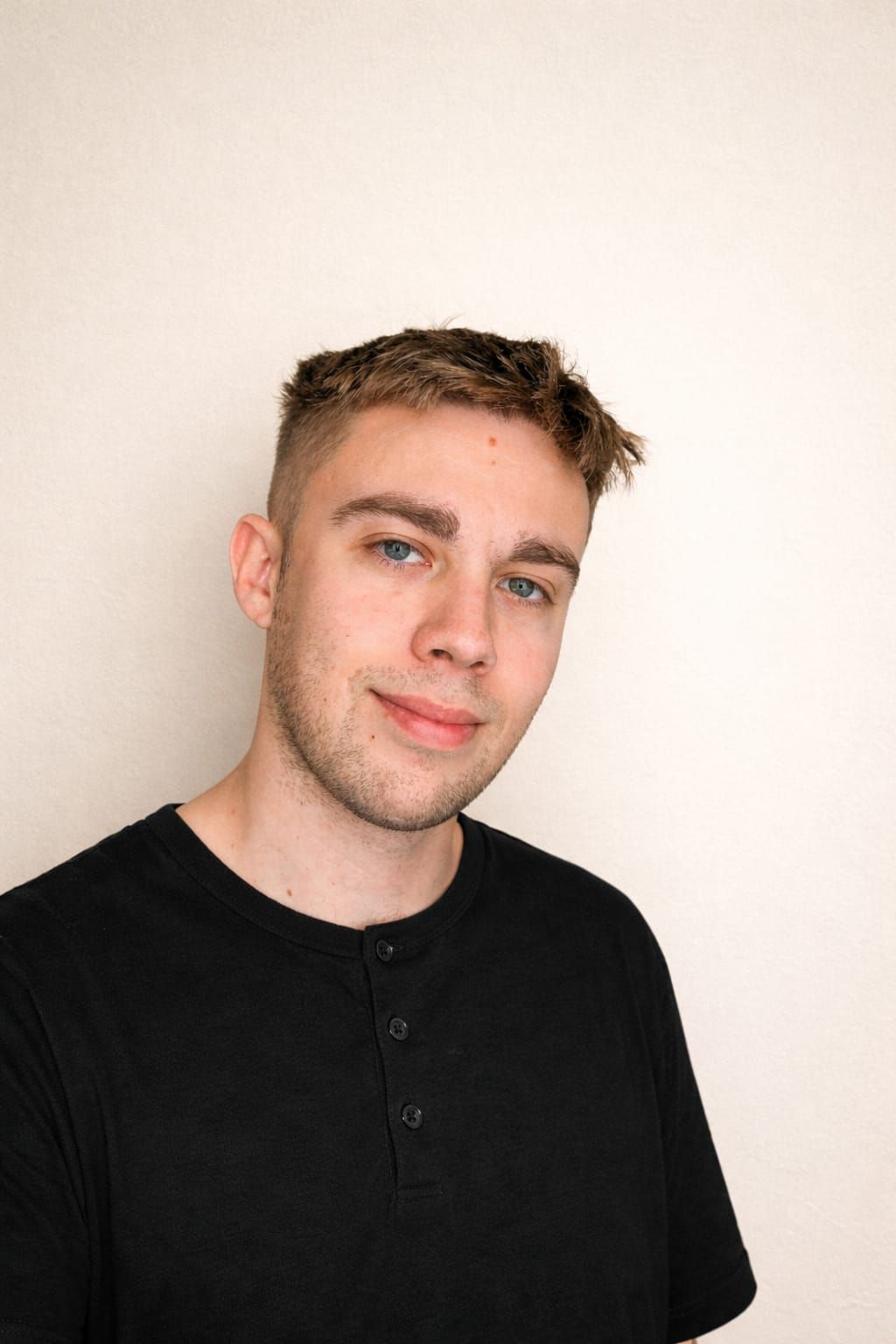 Hombre de pelo corto y castaño, vestido con una camisa negra, sonriendo levemente sobre un fondo blanco.