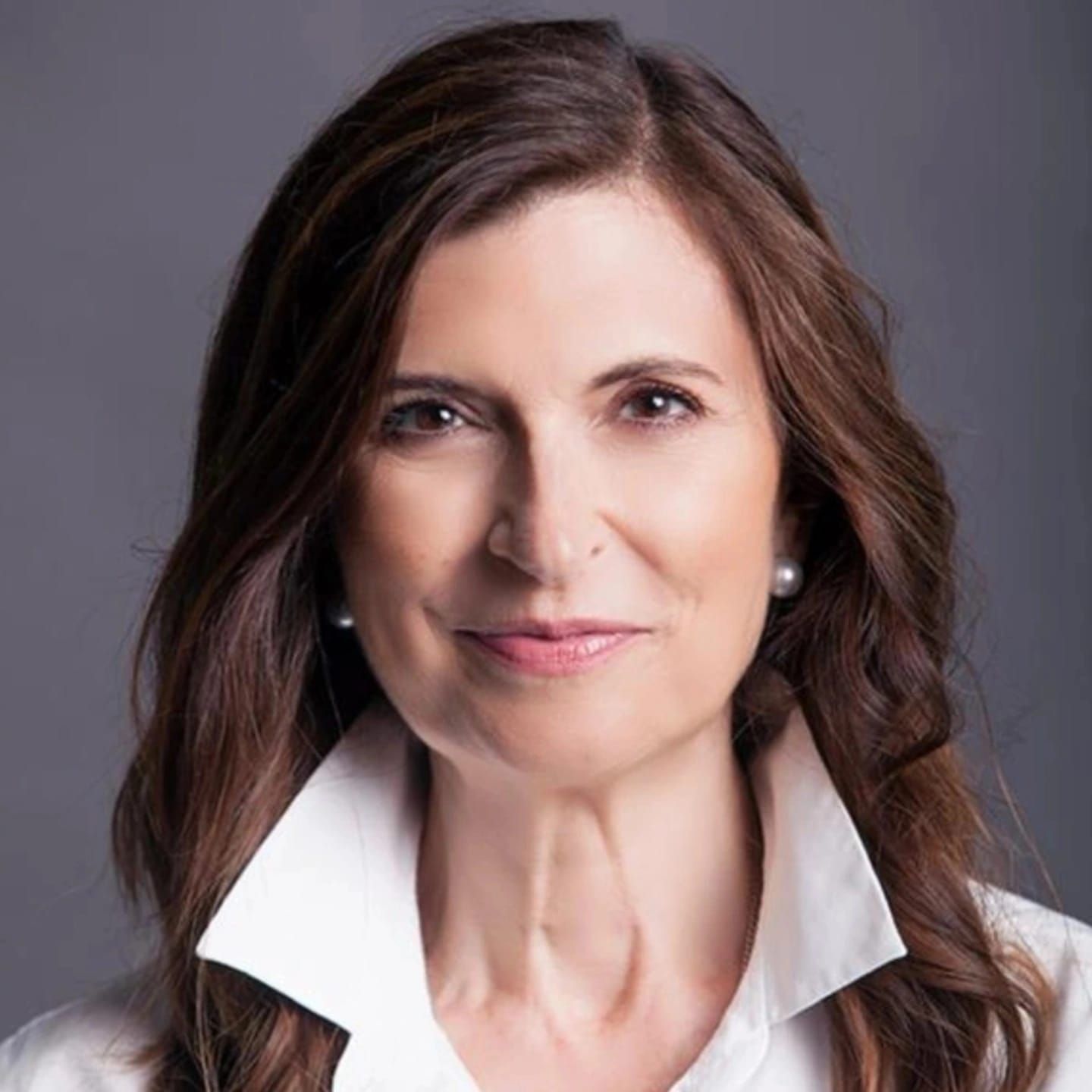 Mujer de cabello largo y castaño, vestida con una camisa blanca de cuello ancho, sonriendo levemente.