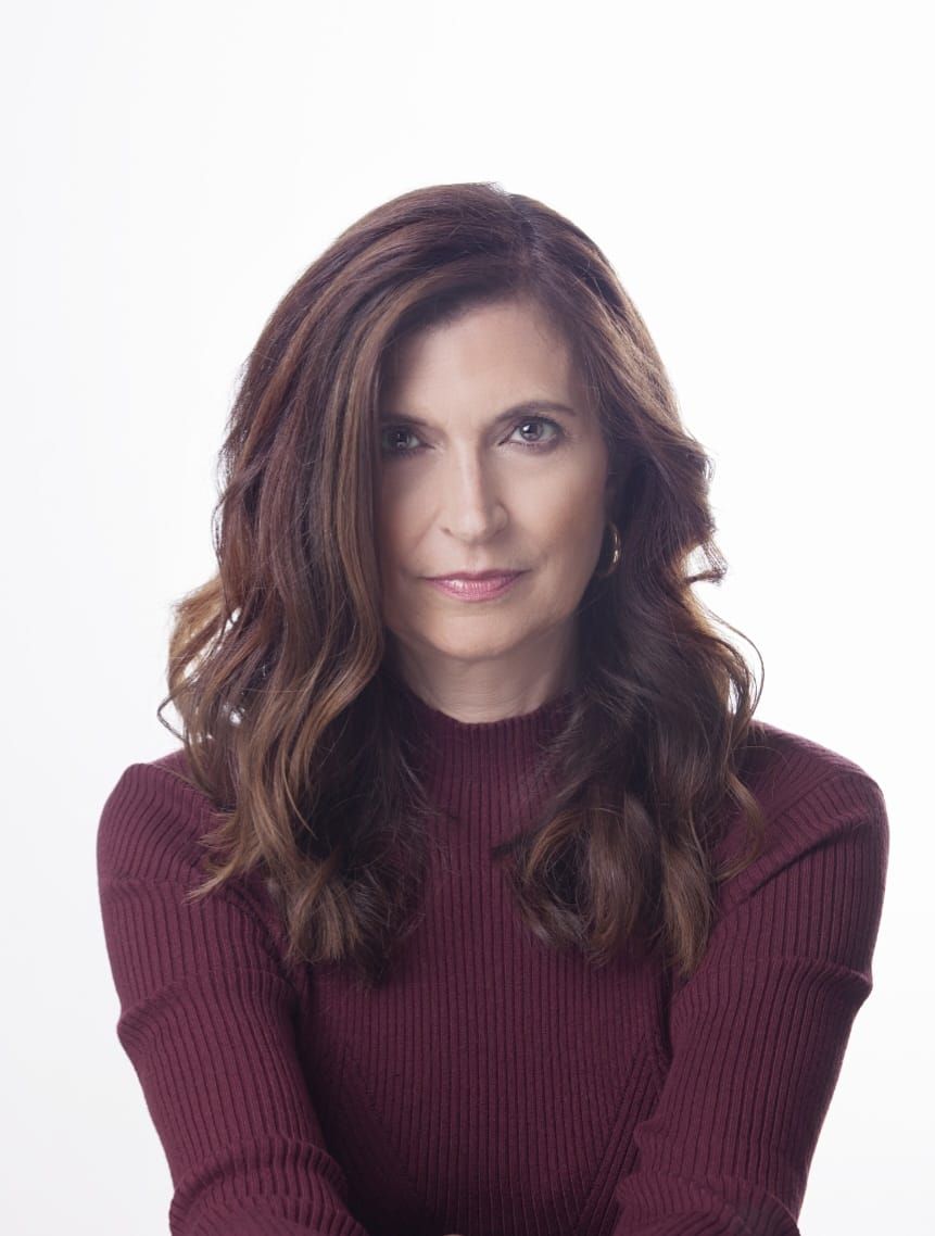 Mujer de cabello castaño con un suéter color burdeos, sonriendo, sobre un fondo blanco.