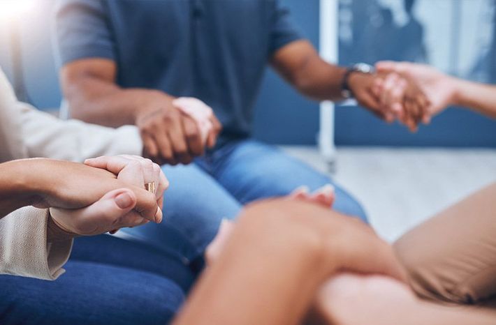 Personas tomadas de la mano formando un círculo de apoyo en un espacio cerrado.