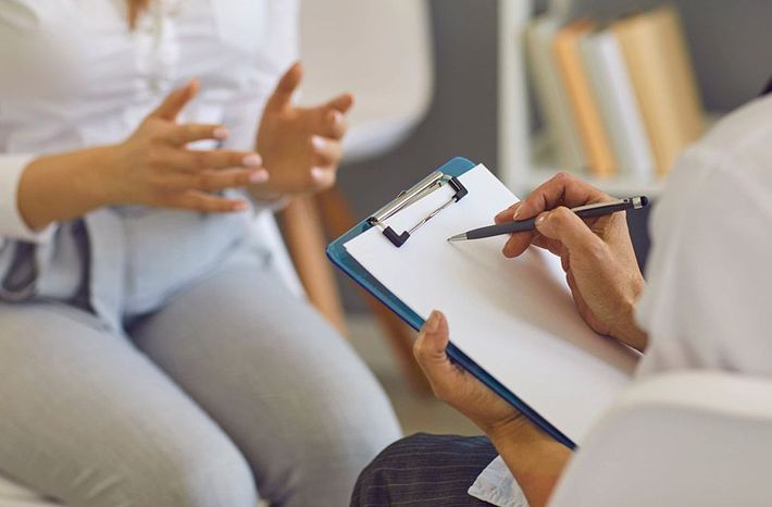 Terapeuta tomando notas durante una sesión de terapia con un paciente sentado.