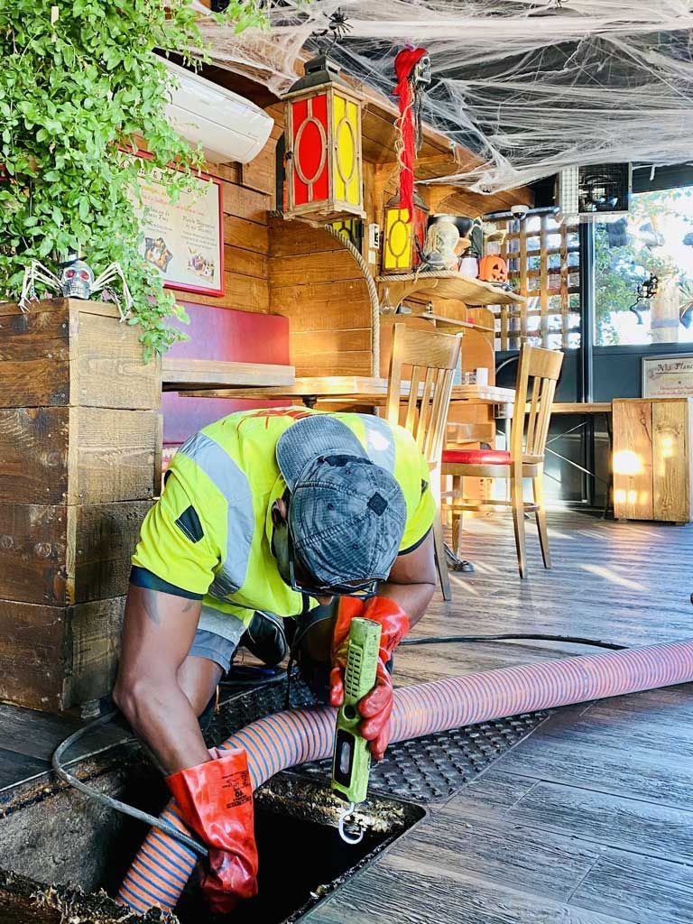 Un ouvrier portant un gilet de sécurité fluo est agenouillé pour réparer des câbles sur un sol texturé dans une salle intérieure faiblement éclairée.