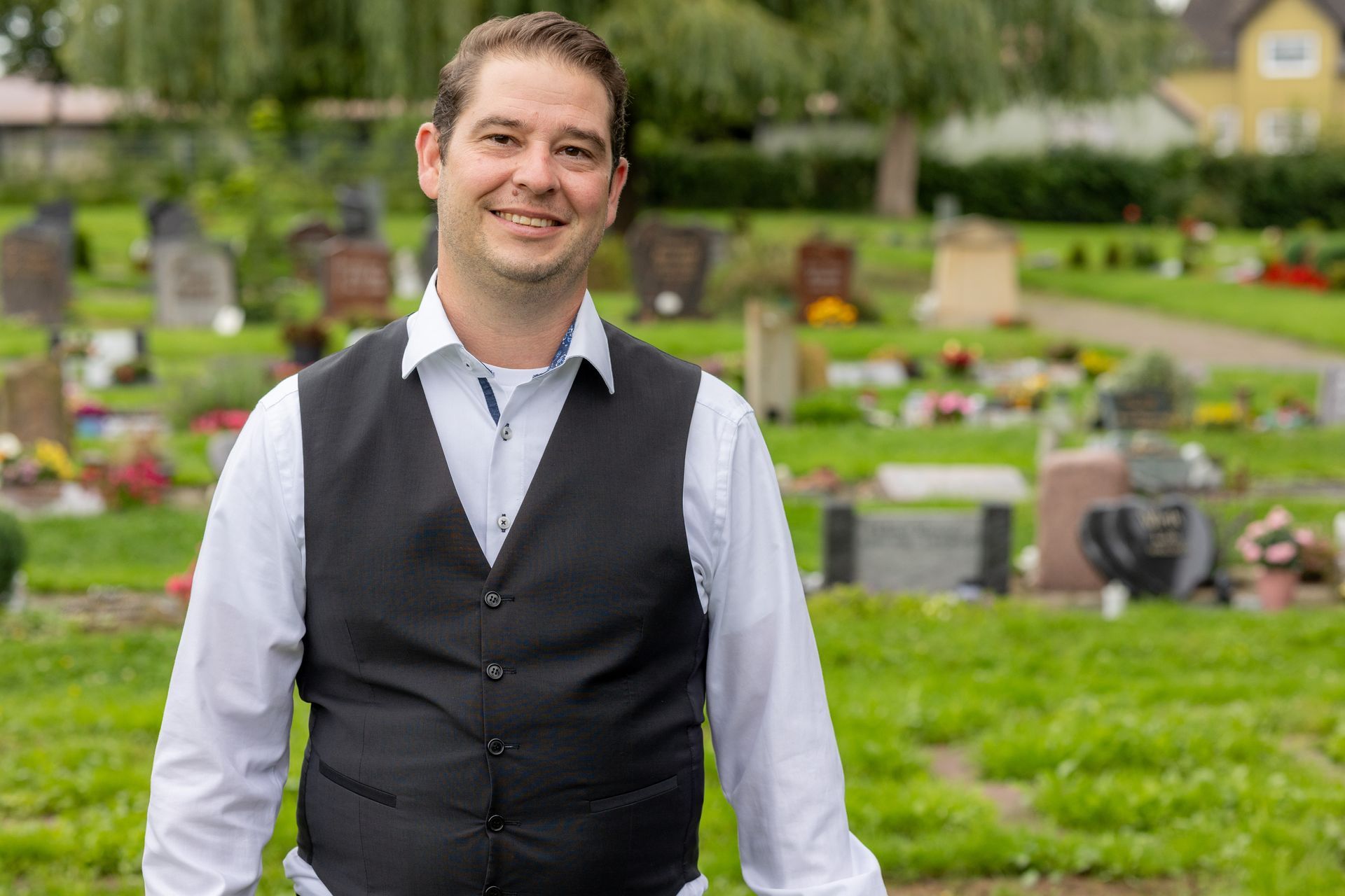 Ein Friedhof mit Blumen und einem Haus im Hintergrund