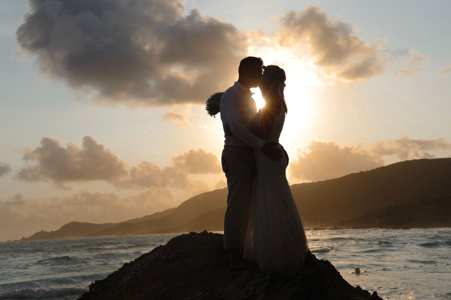 Mariés qui s'embrassent avec le coucher du soleil derrière.