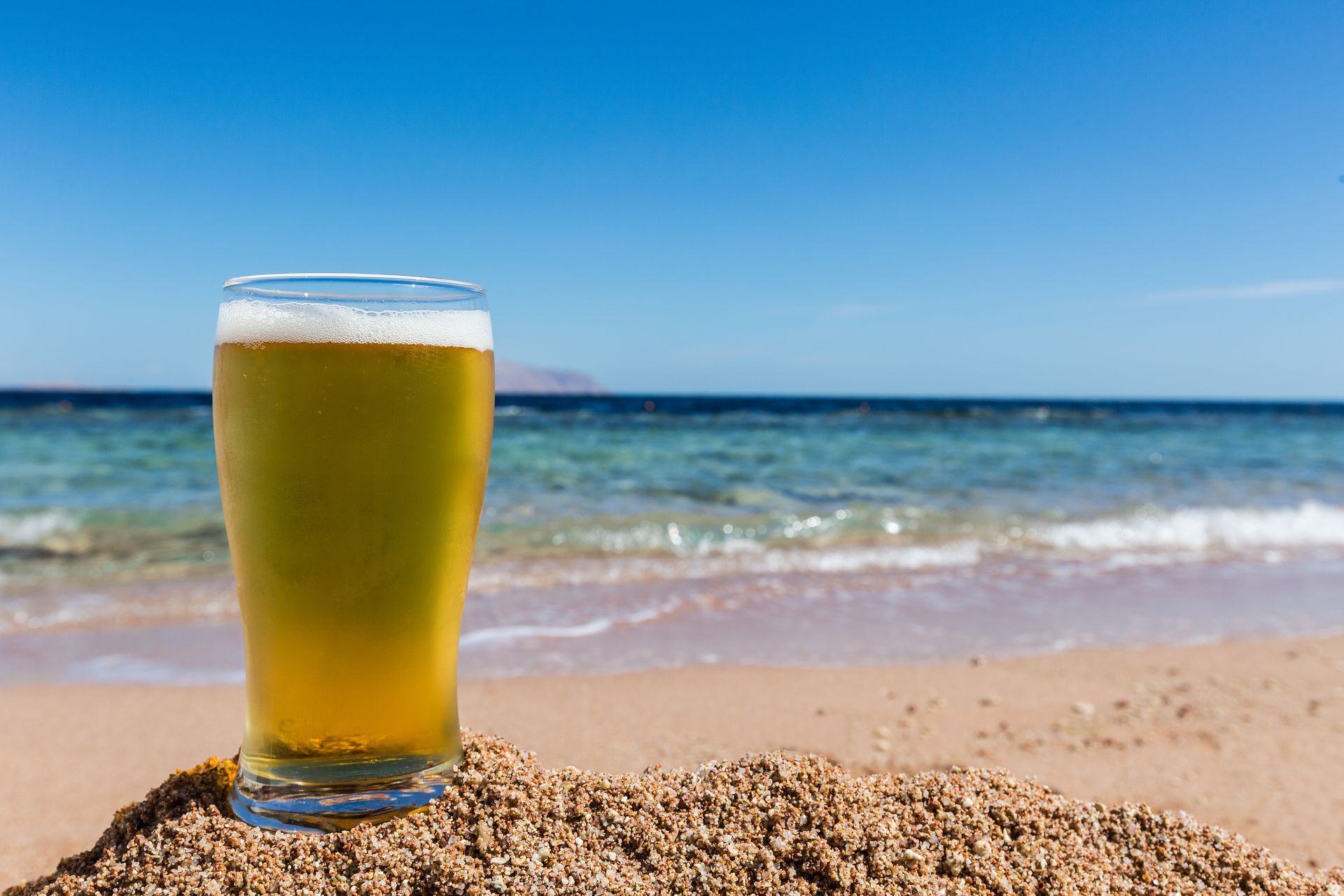 Bière posée sur le sable avec vue sur la mer