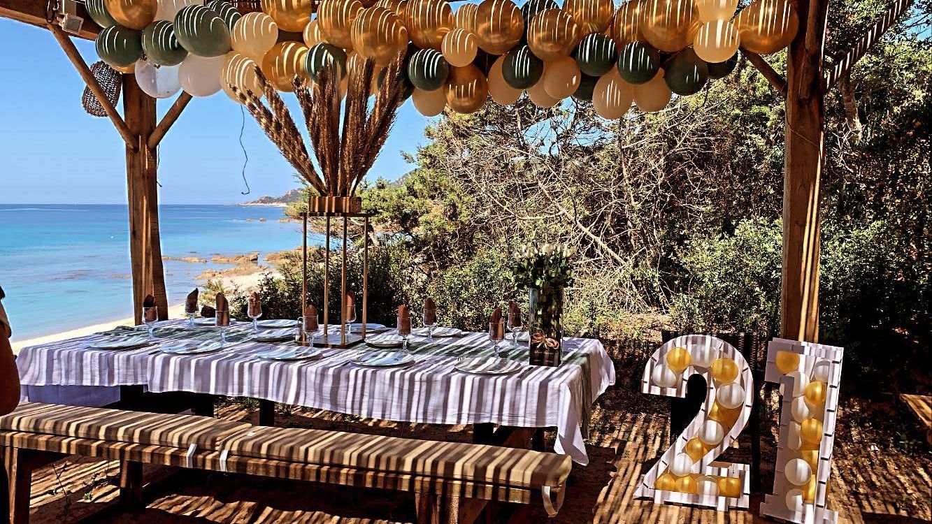 Table dressée pour un anniversaire en extérieur avec des ballons orange et noirs accrochés en hauteur.